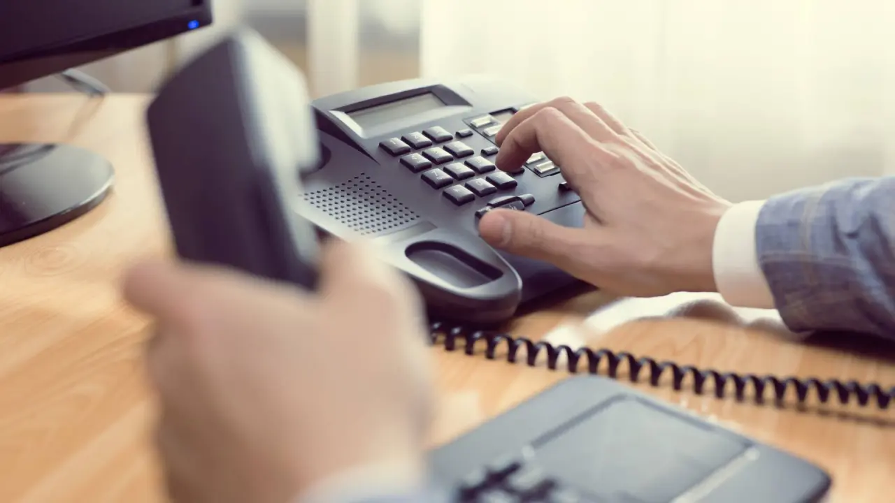 a person’s hand dials numbers on a phone