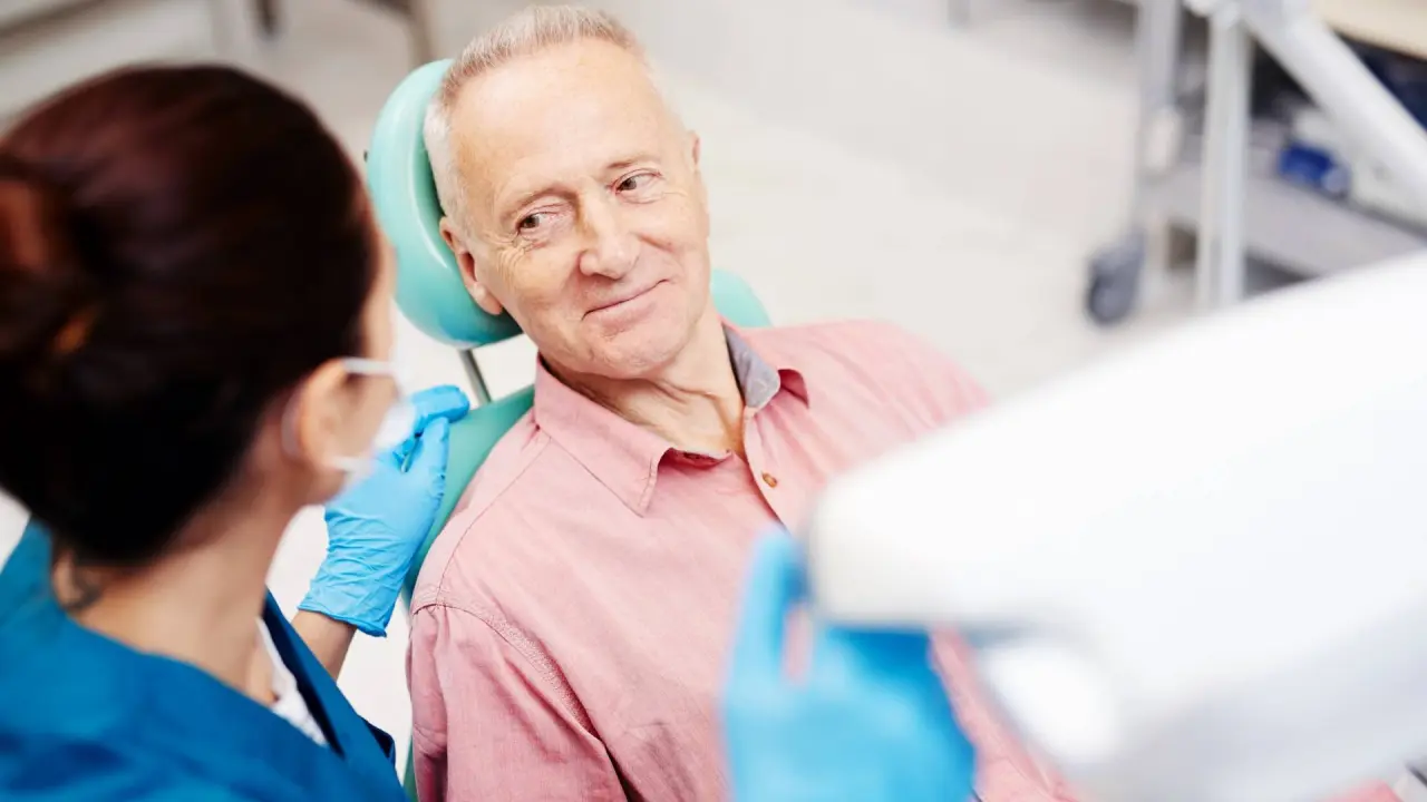 a senior man is looking at his dentist and listening to her advice after an oral check-up