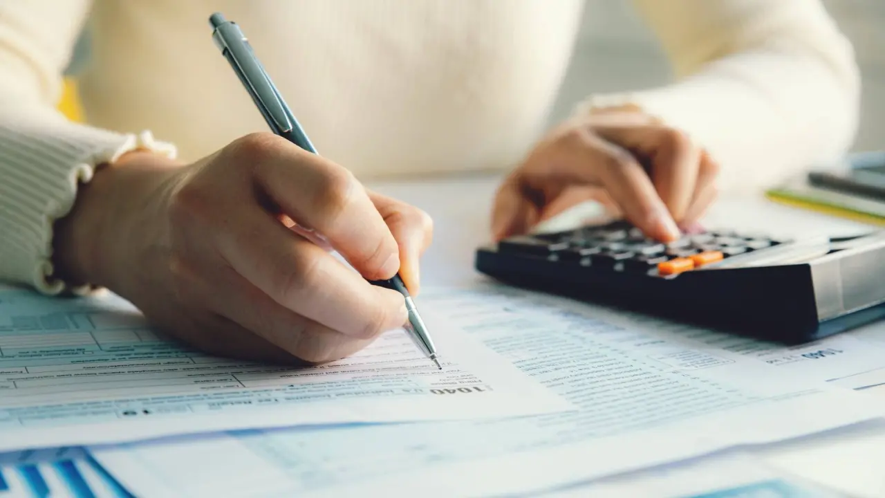 a dentist tries to understand their finances and buying power as they type on a calculator and take notes on tax forms