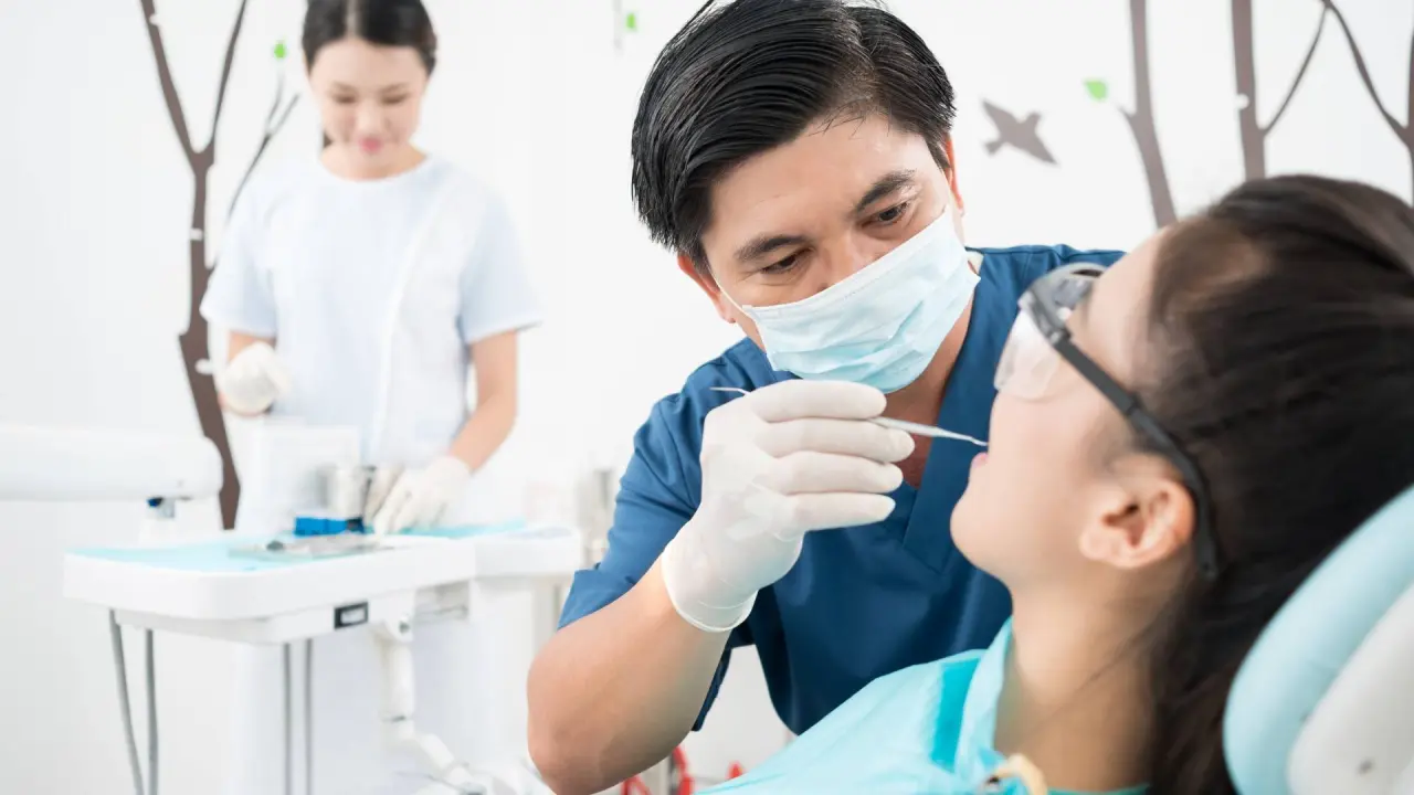 a serious dentist examines a patient while his assistant stands in the background of an established dental practice